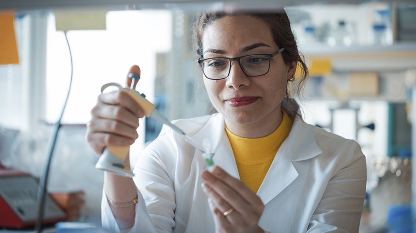 Elham wearing glasses in a white lab coat and yellow shirt in the lab