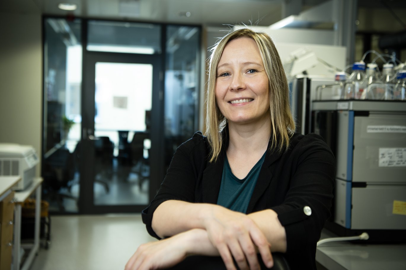 Dr. Nieminen wearing a black sweater and dark green shirt and standing in the laboratory