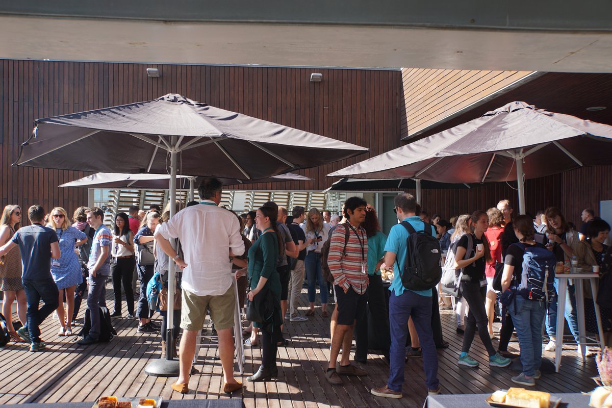 A group of people talking outside under umbrellas with sun shining