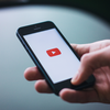 Hand holding a mobile with a YouTube logo visible.