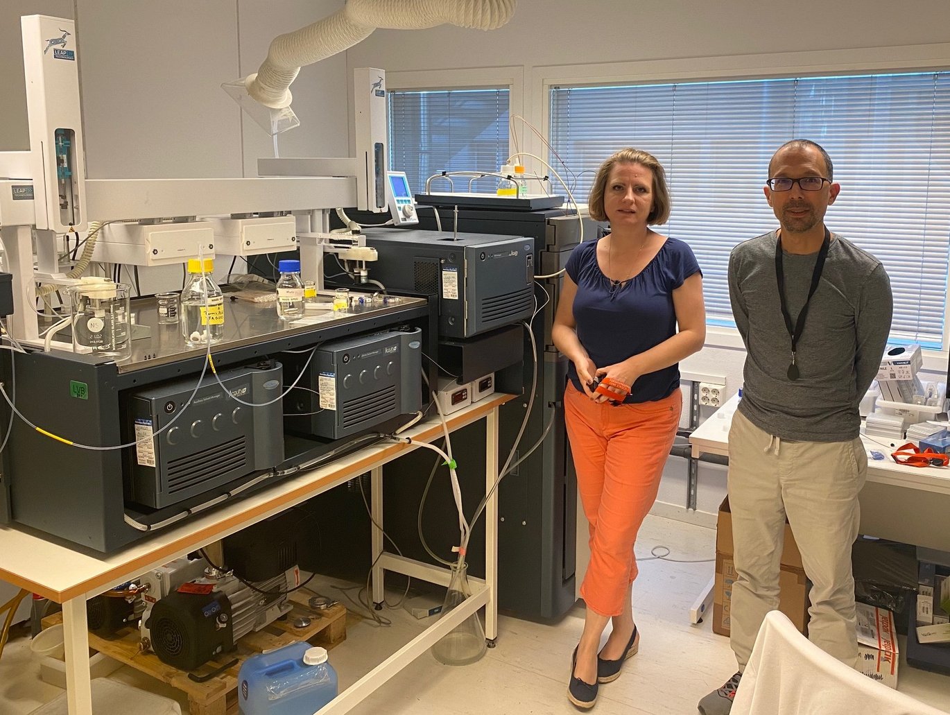 Nikolina Sekulić in a dark top and Dario Segura Peña in a gray sweater standing in the laboratory next to the mass spectrometry instrument