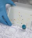 Plastic plate held by a gloved hand on top of experimental data from drug testing