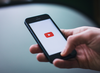 Hand holding a mobile with a YouTube logo visible.