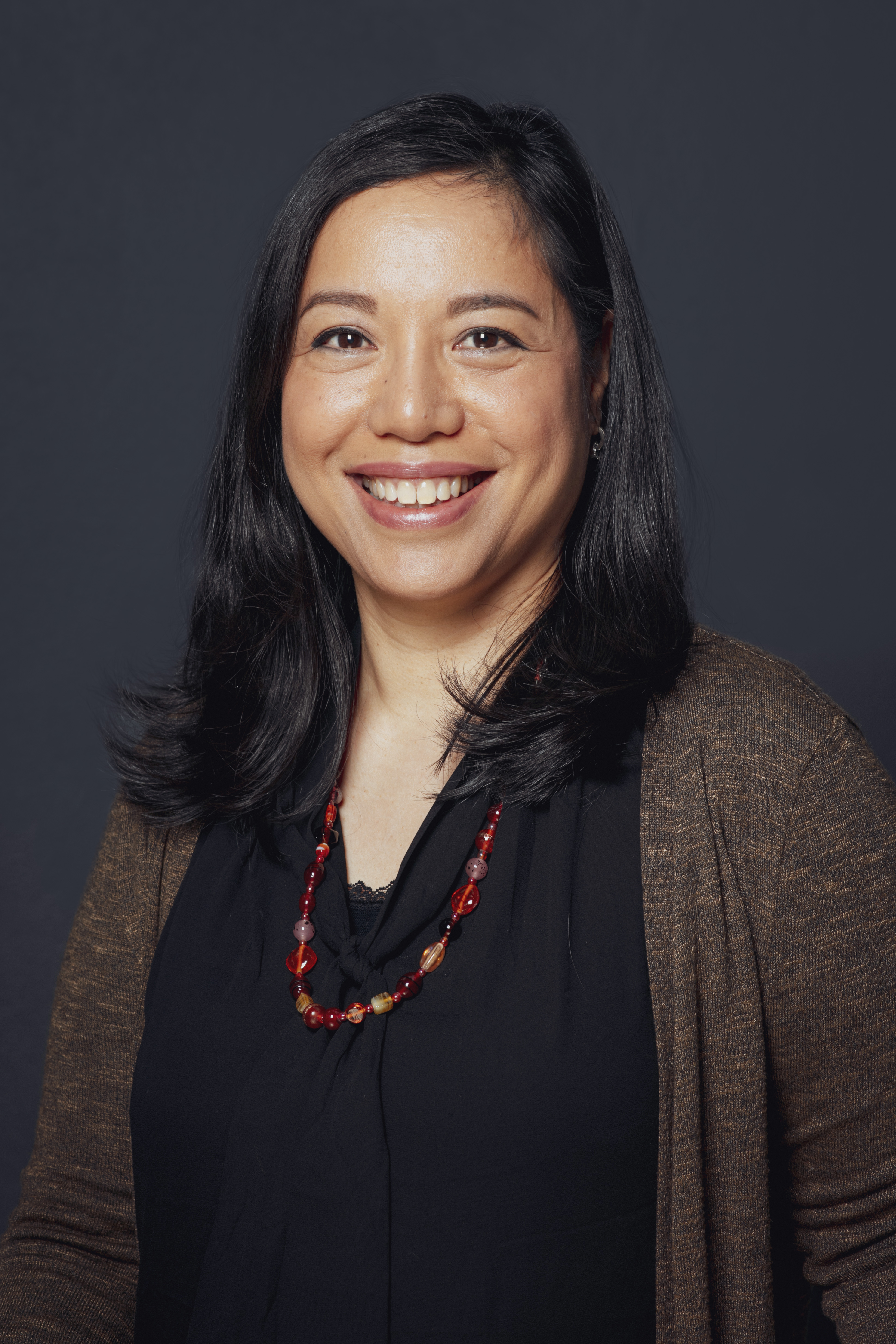 Dr. Camila Esguerra in a black top with brown sweater on a dark background