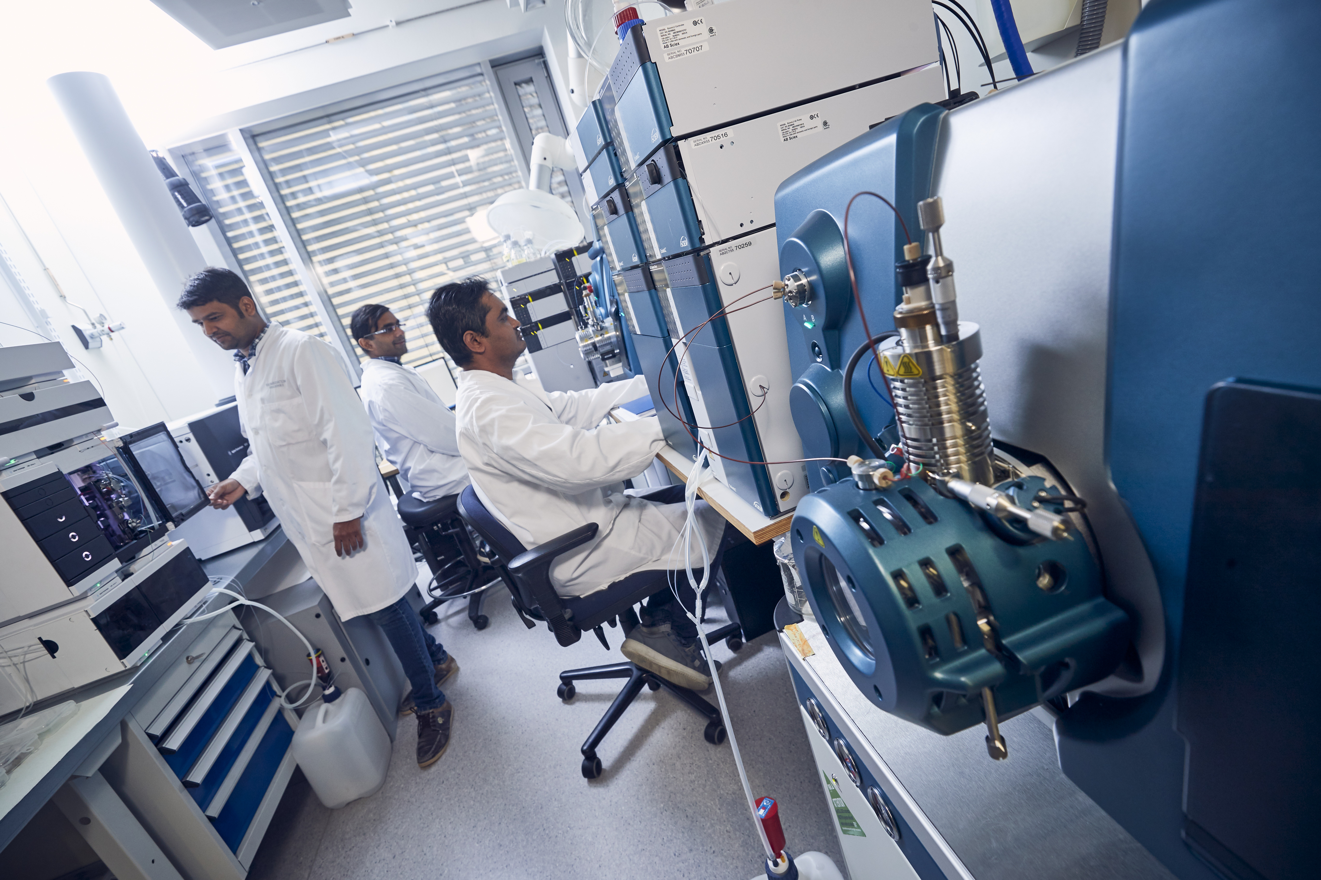 Three people in white laboratory coats working with large laboratory instruments.