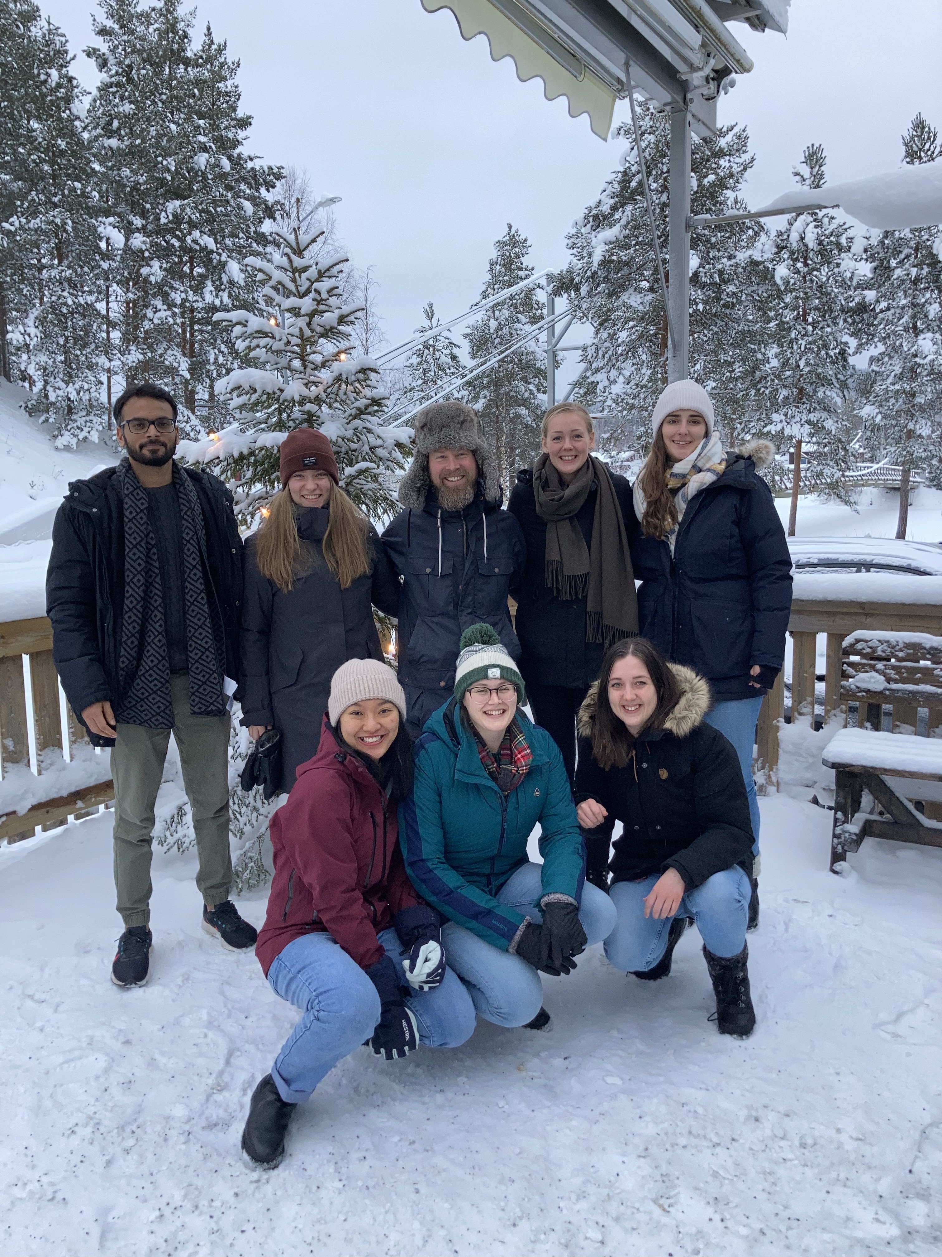 Eight people in coats and hats standing outside with snow on the ground