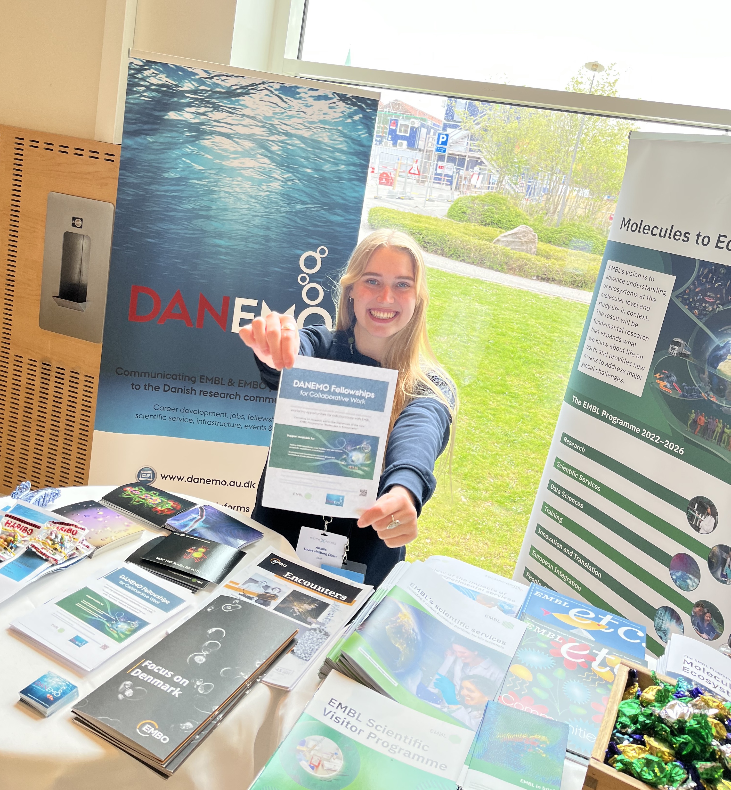 A woman sitting at a table giving out information about EMBL and EMBO