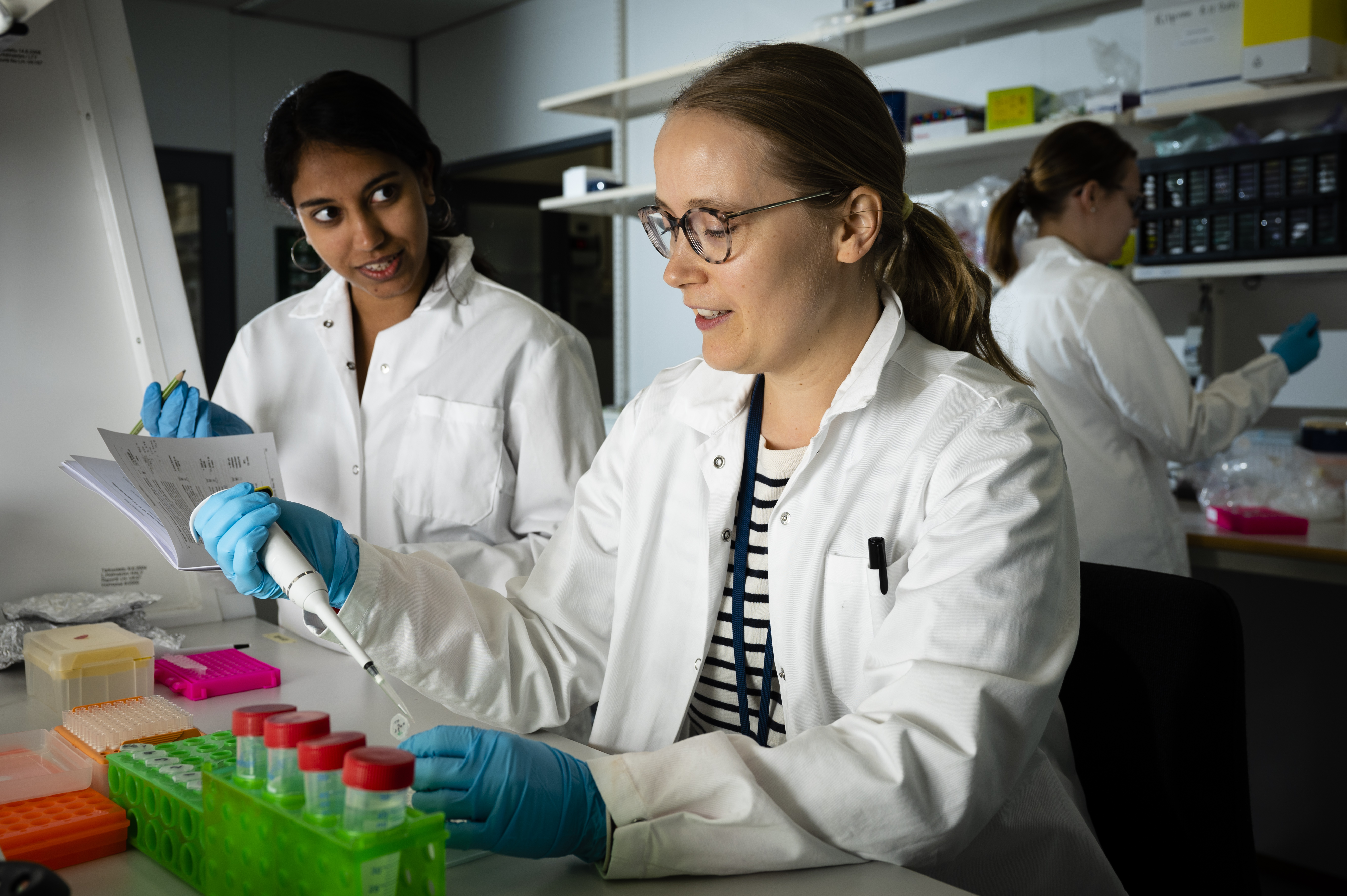 Three people wearing lab coats and gloves and working in a laboratory.