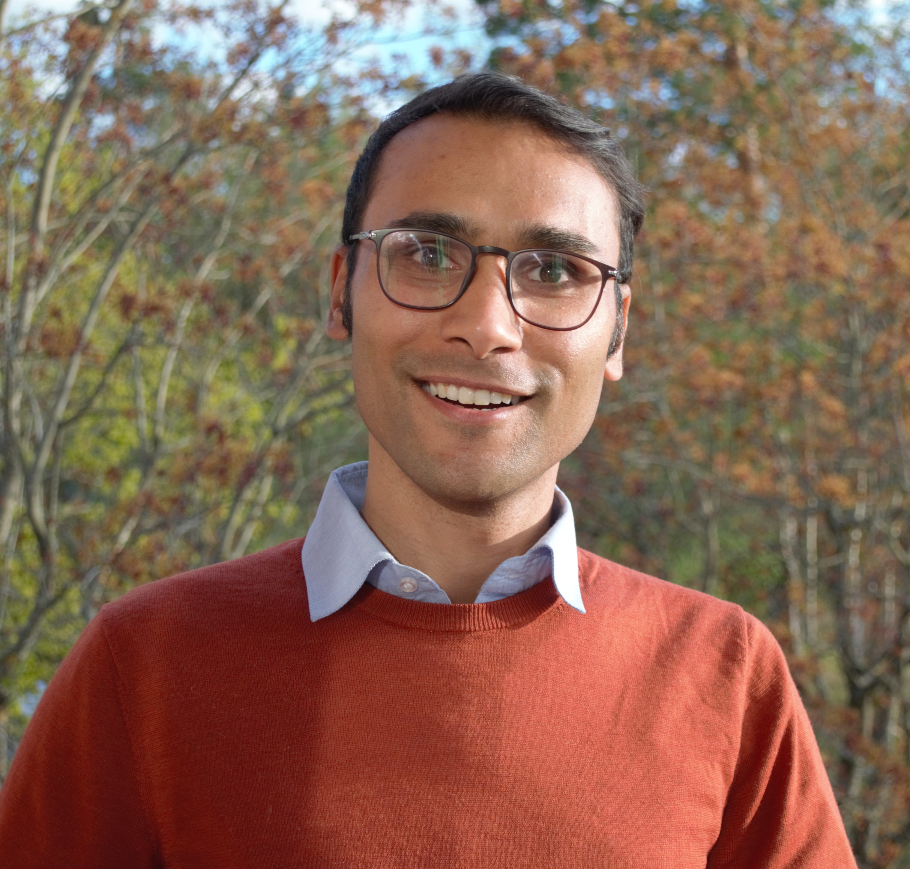 Naresh standing outdoors wearing a dark orange sweater and glasses