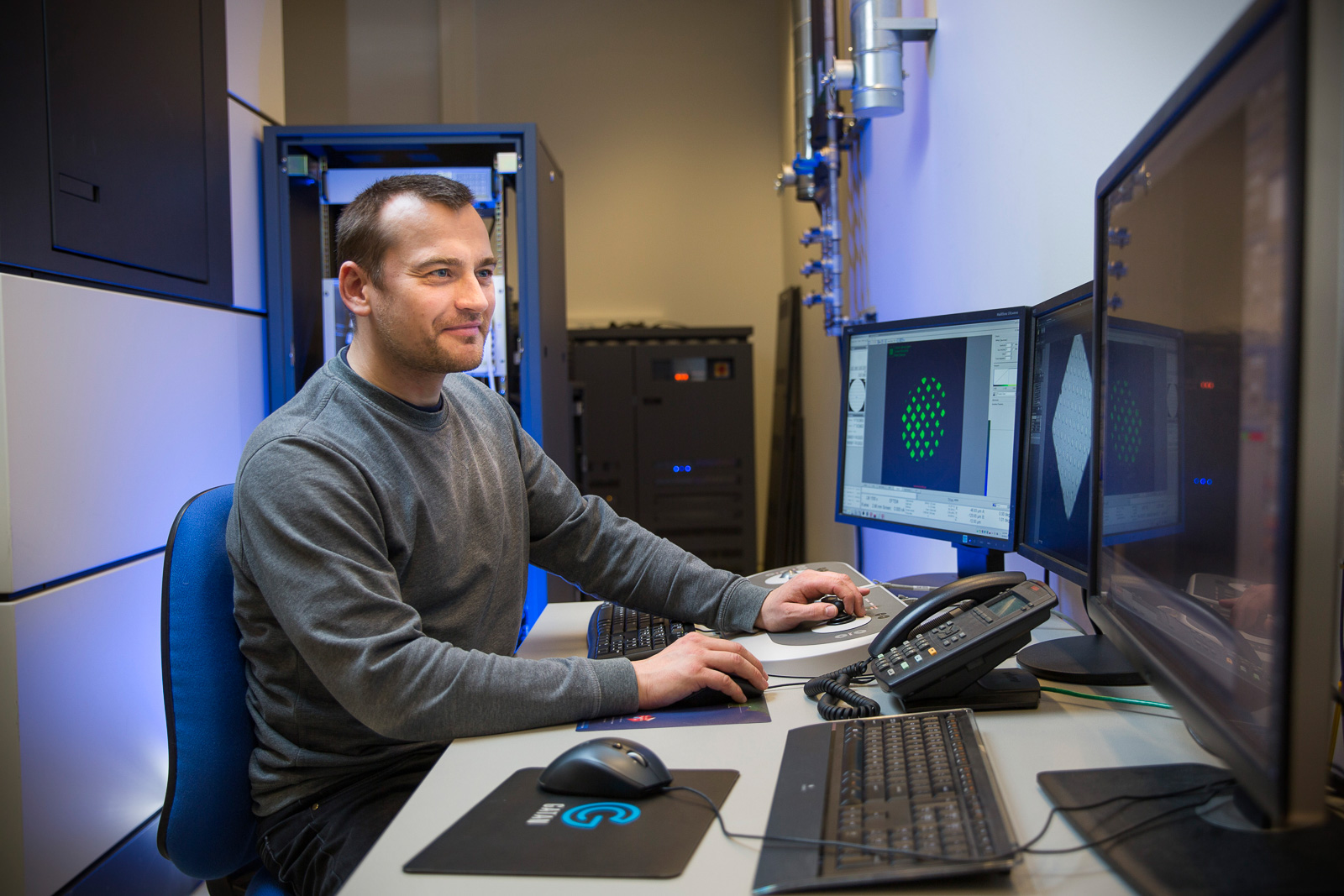 Dr. Thomas Boesen in a gray shirt sitting at a computer with three monitors.