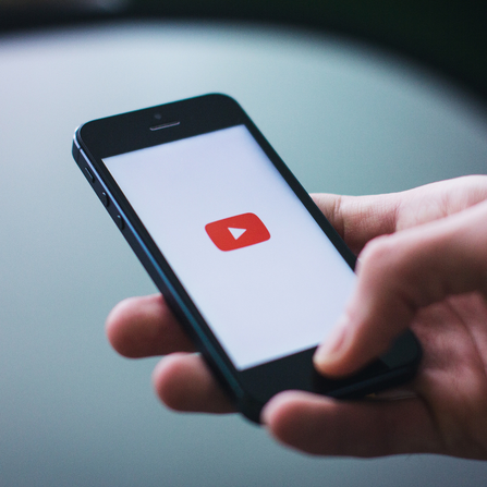 Hand holding a mobile with a YouTube logo visible.